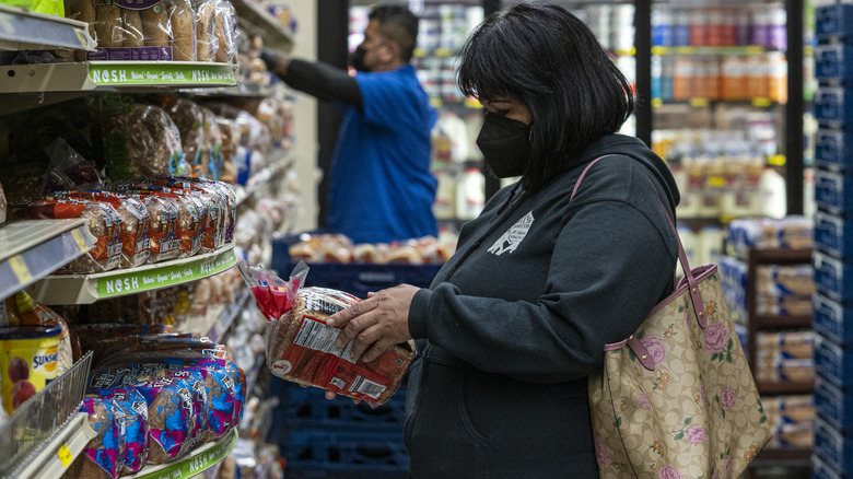 woman looking at a loaf of bread in grocery store