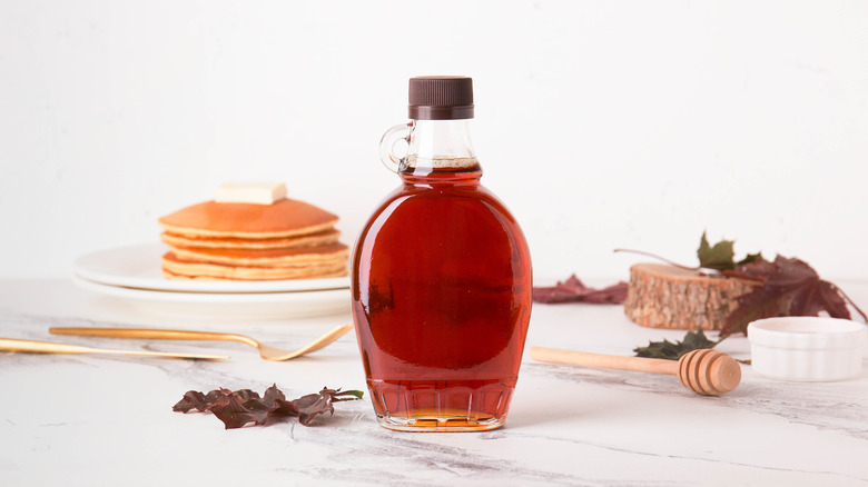 Jar of authentic maple syrup with pancakes in background