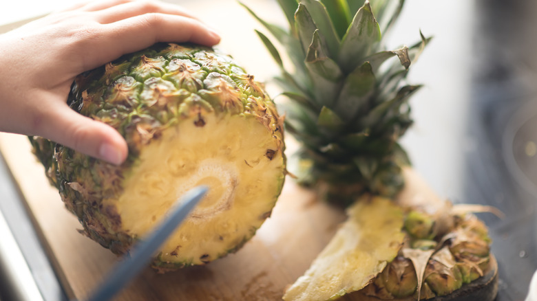 Hand holding down a pineapple with knife to cut it