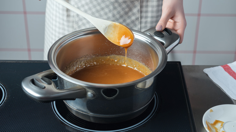 Person in checkered apron making caramel sauce in pot