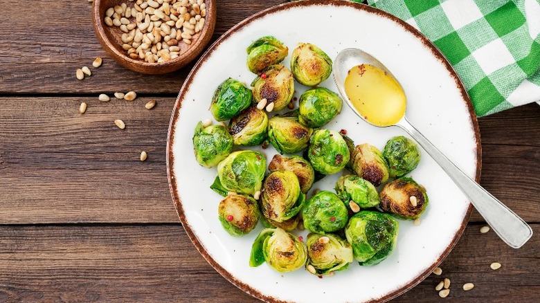 Roasted Brussels sprouts on a plate with a bowl of pine nuts