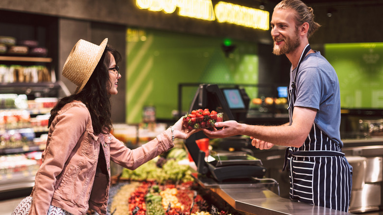 A grocery shopper handing strawberries to an employee