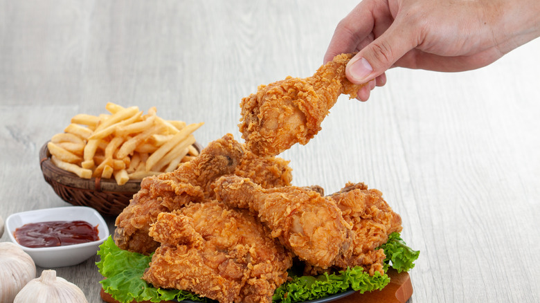 Person taking a fried chicken wing from plate of fried chicken with side of fries