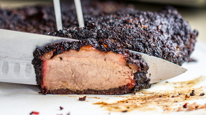 Knife slicing charred and smoked brisket