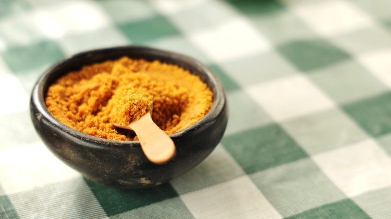 unrefined brown sugar in black ceramic bowl over green gingham background