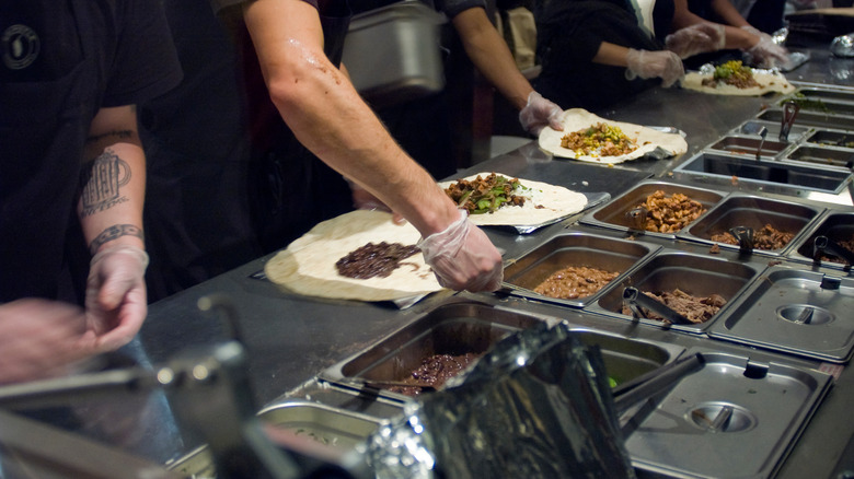 People in black making Chipotle burritos