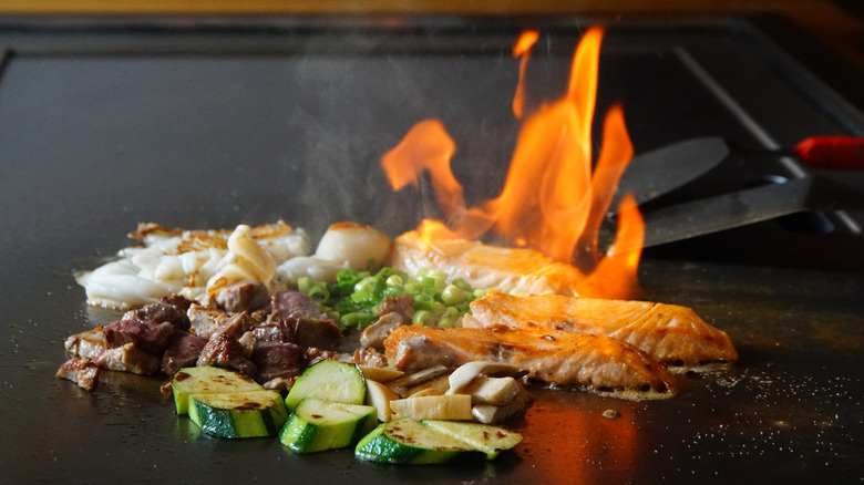 hibachi meat and veggies flaming on griddle with spatulas