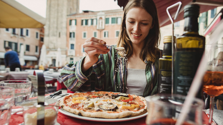 Woman sprinkling cheese on Italian pizza in outdoor restaurant