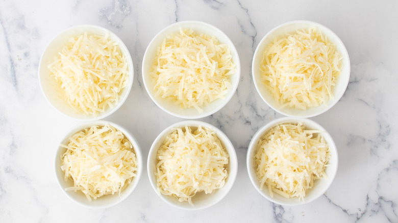 six white bowls with shredded cheese