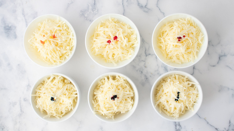 six white bowls with shredded cheese and drop of food coloring