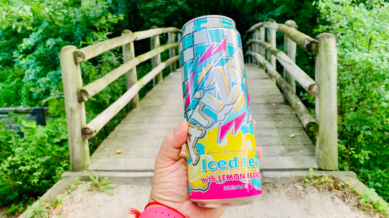 A brightly colored can of Lemon AriZona Iced Tea in front of a foot bridge