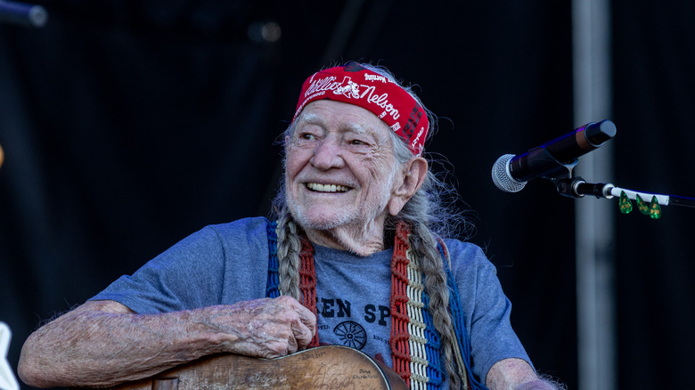 Willie Nelson wearing red bandana and smiling on stage