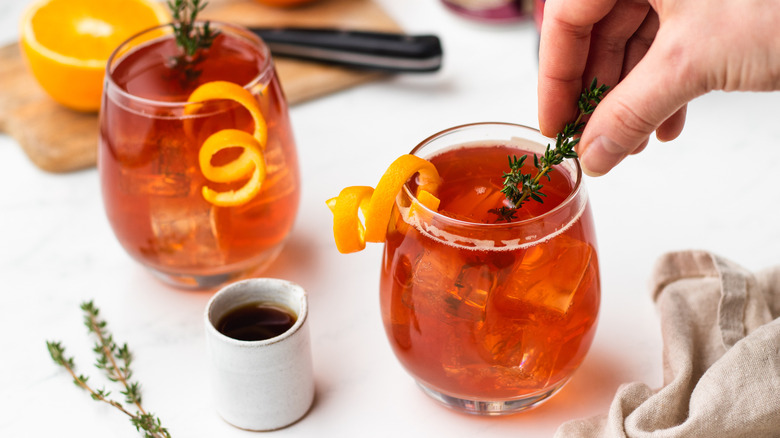 Two cranberry cocktails garnished with thyme and orange