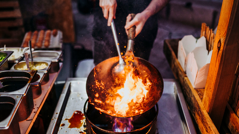 chef cooking in a wok over open flame