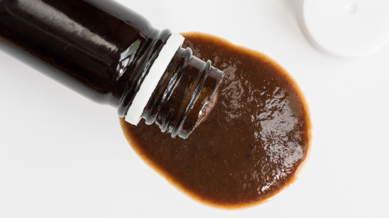 Brown steak sauce pouring out from dark bottle.