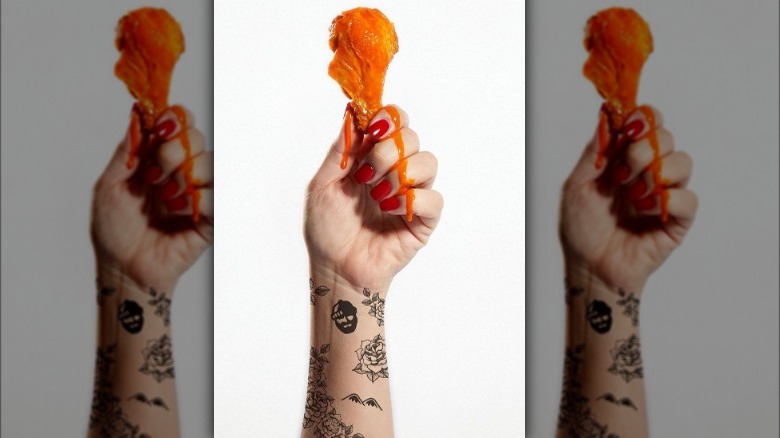 Arm with tattoos holding a chicken wing