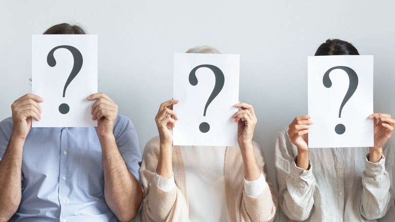 Three people holding papers in front of faces