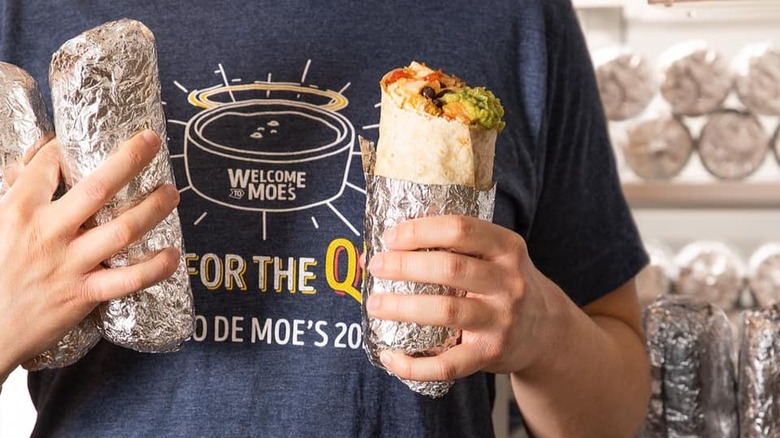 Moe's employee holding wrapped burritos