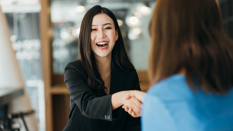 A smiling woman shaking someone's hand.