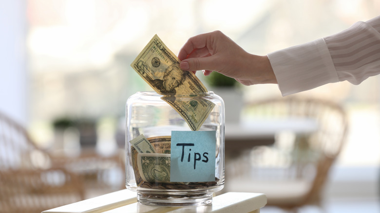 Person placing a $20 bill in a tip jar.