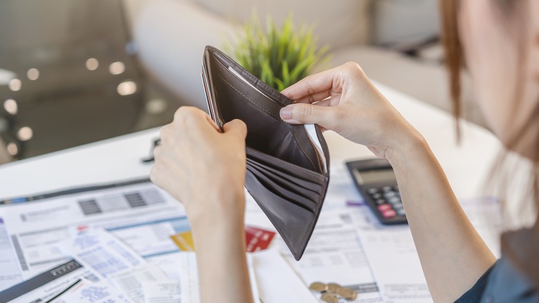 Person looking into empty wallet next to pile of bills