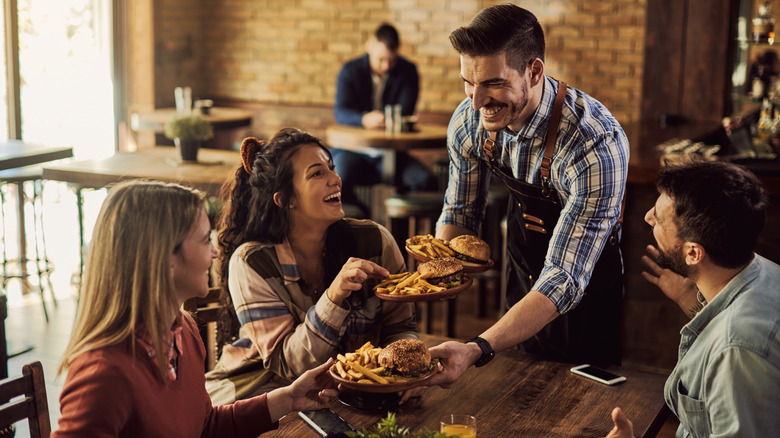 Server passing out meals at a table full of cheerful customers