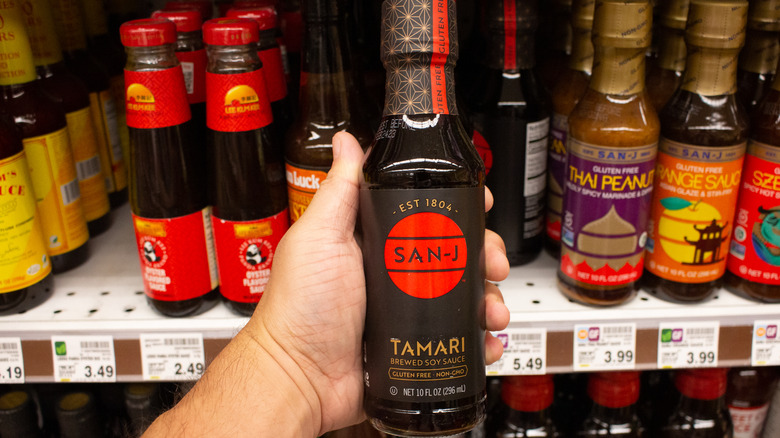 Hand holding a dark bottle of tamari