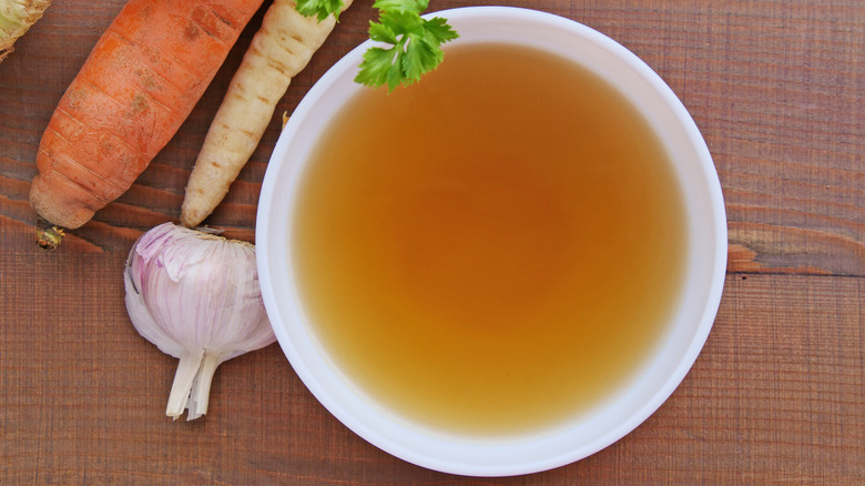 Vegetable Broth in a bowl next to garlic, carrot, and parsnip