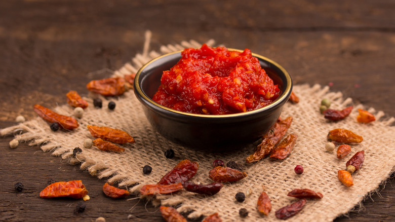 Metal bowl with sambal oelek surrounded by peppers