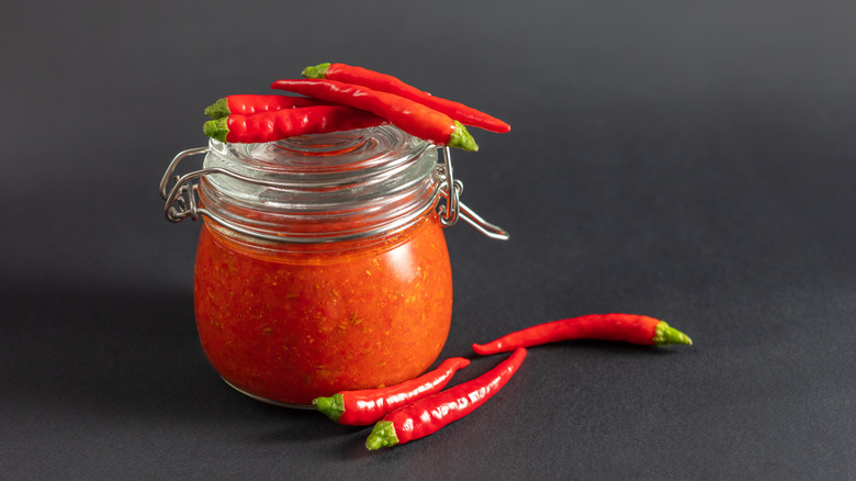 Harissa sauce in glass jar with lid and peppers on top