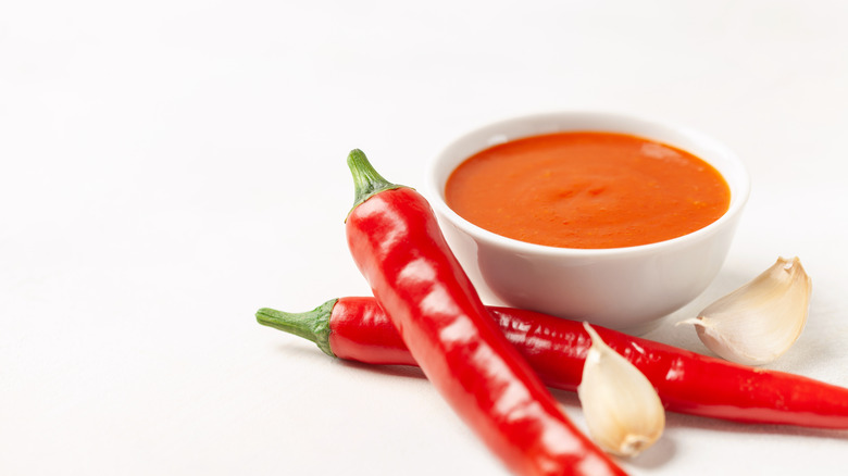 Bowl of orange sauce next to peppers