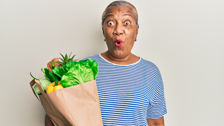 shocked woman holding bagged groceries 