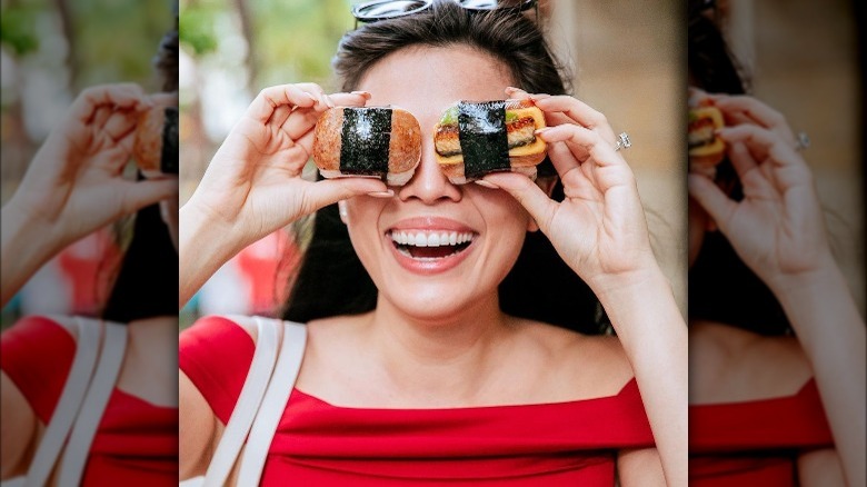 Woman holding spam musubi over her eyes