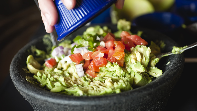 adding fresh vegetables to guacamole