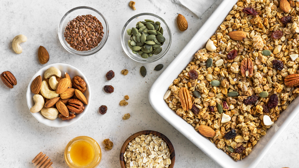 Granola in a white baking dish next to bowls of nuts