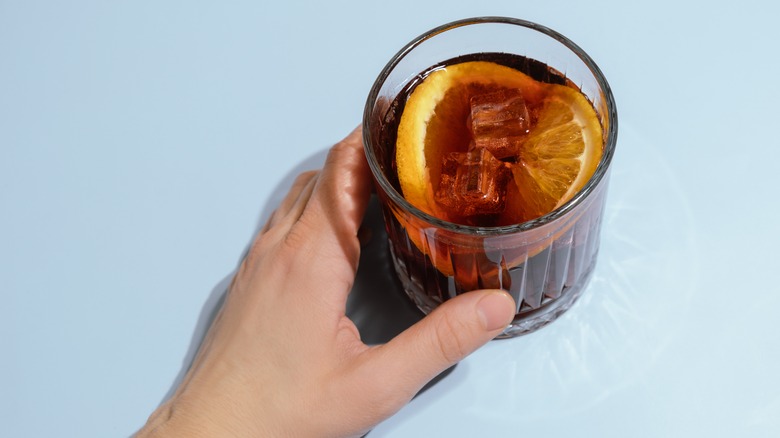 Hand holding tumbler with negroni sbagliato