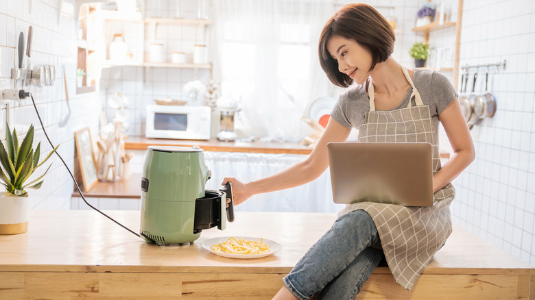 Woman in apron using an air fryer while on laptop