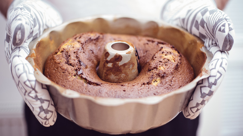 Hands in oven mitts holding a bundt cake tin