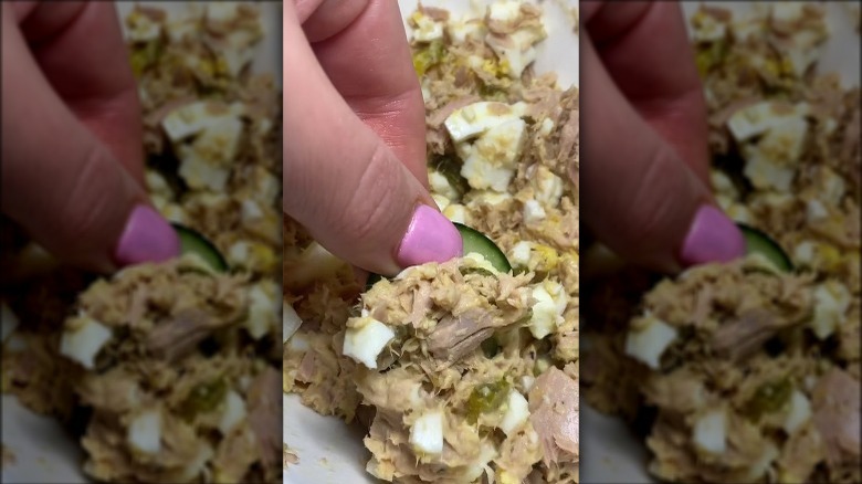 hand dipping a cucumber into tuna and egg salad