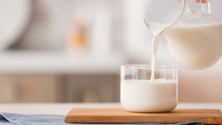 Pitcher of milk pouring into a glass on wood block