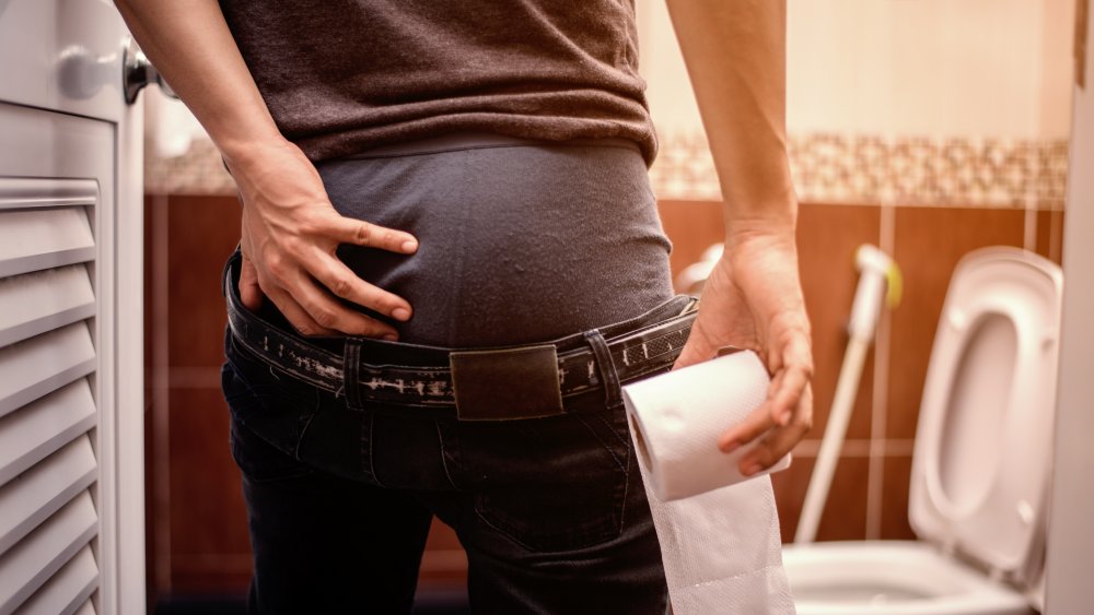 Man holding roll of toilet paper in bathroom