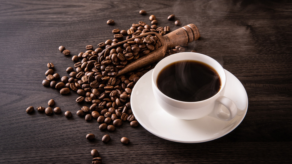 A cup of coffee in a white cup with coffee beans 