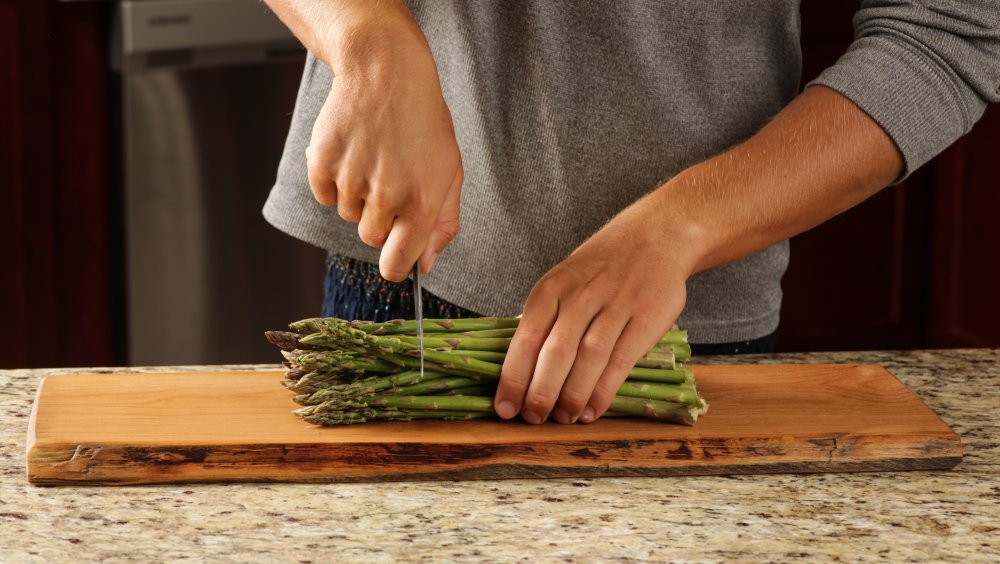 Person chopping asparagus on a wooden cutting board