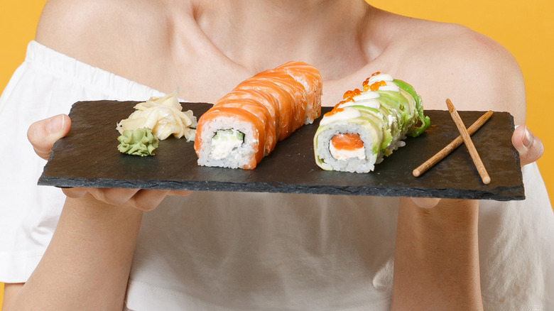 Woman holding black slab with sushi and chopsticks