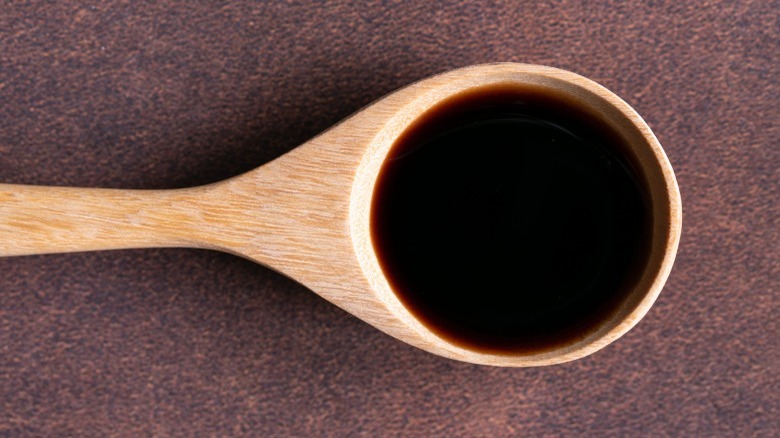 Wooden tablespoon with vanilla extract on brown background