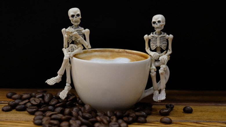 Two toy skeletons sitting on a cup of coffee