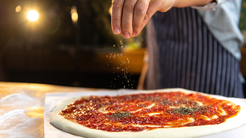 Chef sprinkling oregano on pizza