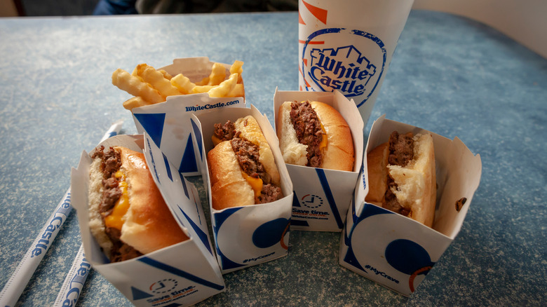 Several White Castle hamburgers, crinkle fries and a drink on a table