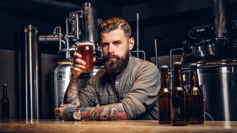 Tattooed man holding glass of beer in brewery