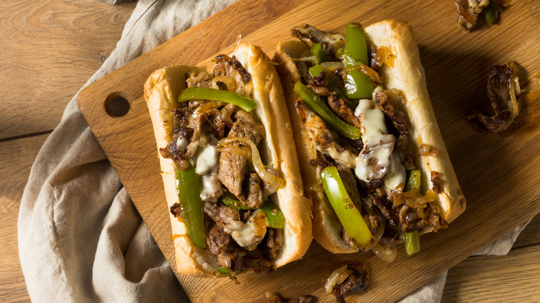 Philly cheesesteak sandwich with green peppers on wooden platter